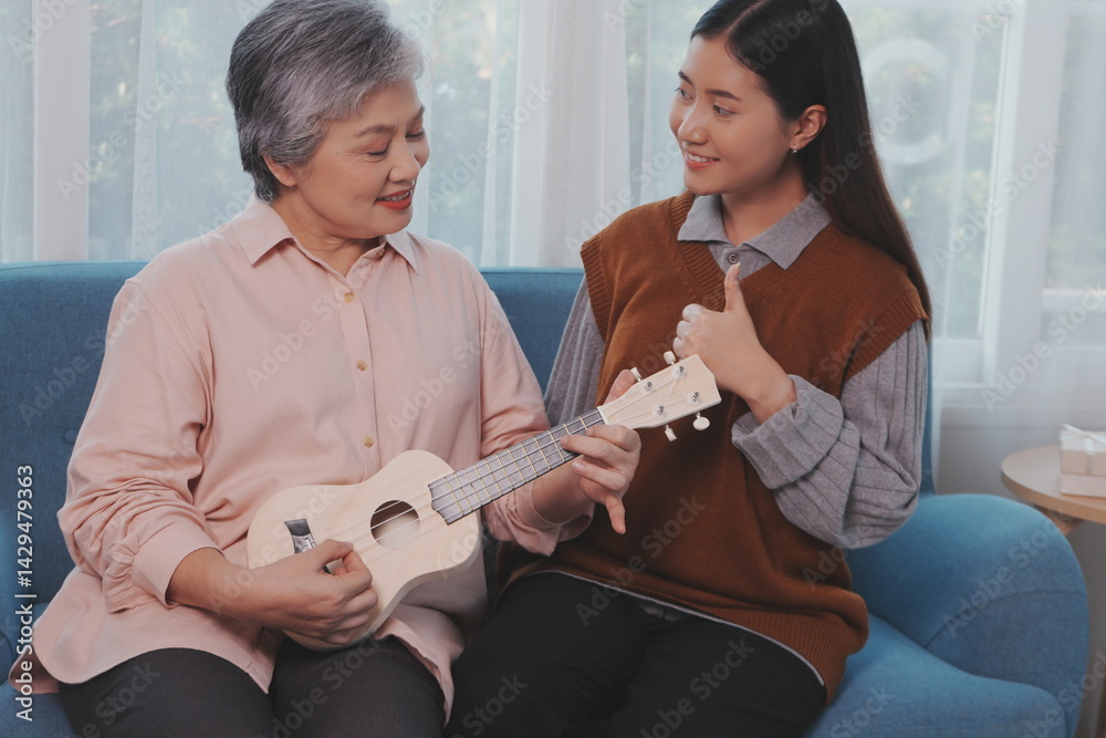 Asian elderly mother and her beautiful 29-year-old daughter relax on the sofa playing ukulele happily together at home.