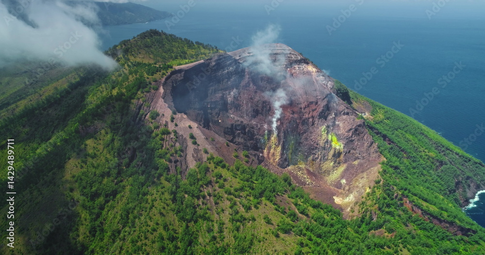 White smoke billowing from the crater of Mount Iliwerung volcano on Flores Island, Indonesia, surrounded by lush green vegetation and the blue ocean