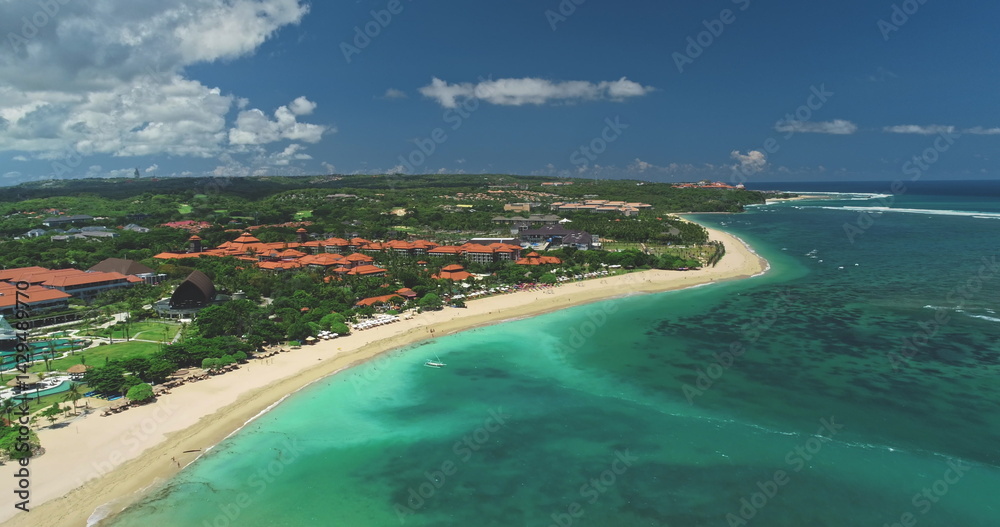 Capturing stunning aerial views of Nusa Dua beach in Bali, showcasing white sand, luxury hotels, lush greenery, and vibrant turquoise waters under a clear sky