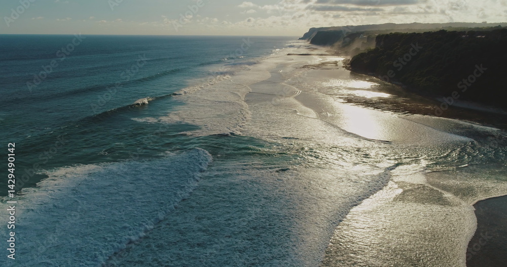 Golden hour sunlight reflecting on the ocean surface, creating a mesmerizing spectacle as gentle waves crash against the shore in an aerial view of a pristine beach