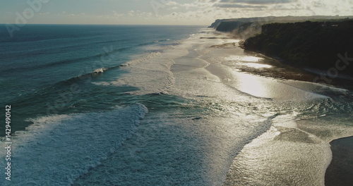 Obraz na płótnie Golden hour sunlight reflecting on the ocean surface, creating a mesmerizing spectacle as gentle waves crash against the shore in an aerial view of a pristine beach w salonie