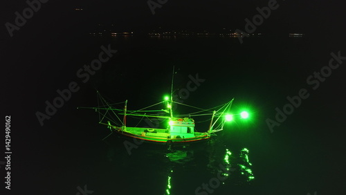 Obraz na płótnie Aerial view of a fishing boat using green lights for night fishing, creating a mesmerizing scene with the reflection on the water and the distant lights of Koh Phangan island in the background w salonie