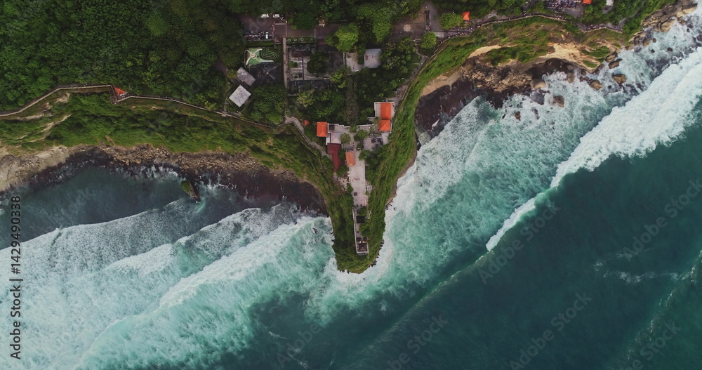 Turquoise waves crashing against the cliff where Uluwatu Temple is perched, revealing a breathtaking panorama of Bali's stunning coastline and vibrant natural beauty