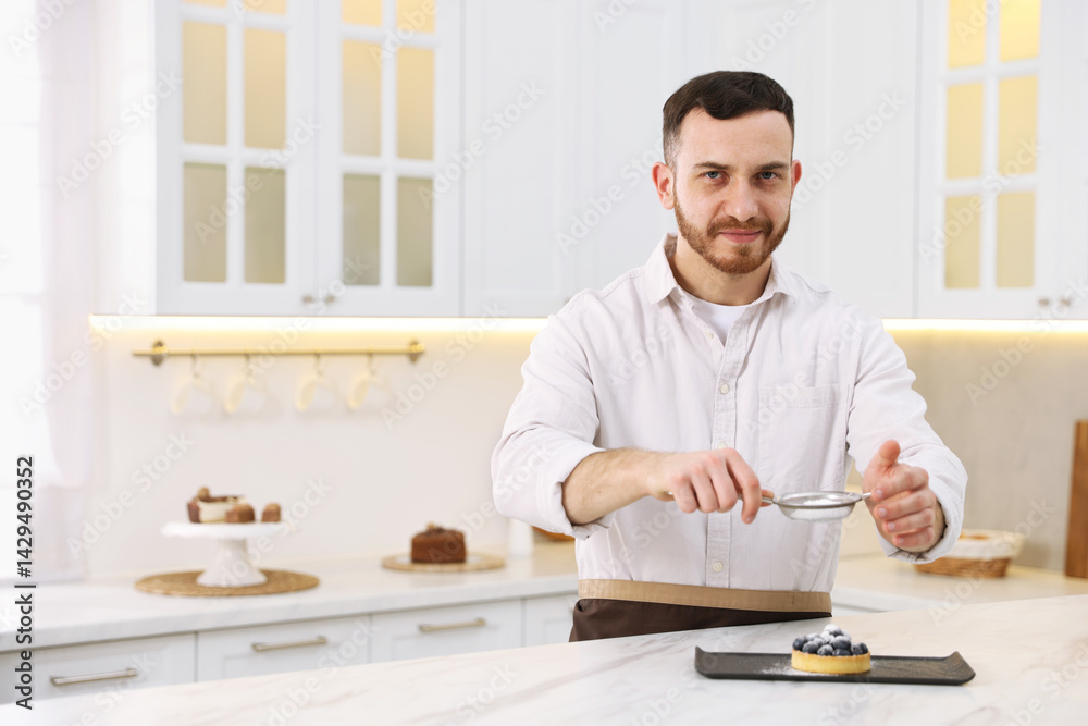 Confectioner sprinkling powdered sugar onto tart at white marble table in kitchen, space for text Confectioner sprinkling powdered sugar onto tart at white marble table in kitchen, space for text