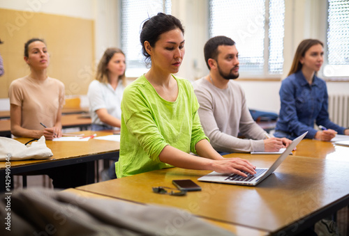 Asian girl is a student engaged on a laptop during classes, studying in a university auditorium with a group