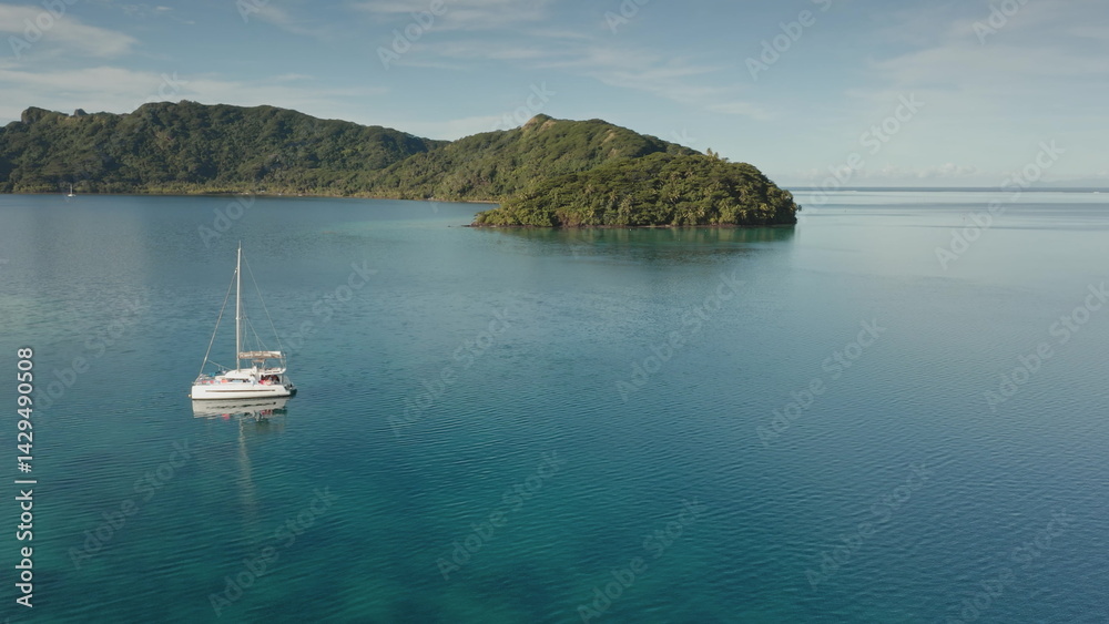 Aerial view of a white catamaran sailing on calm turquoise water near a lush green tropical island in Bora Bora, French Polynesia, creating a serene and idyllic scene