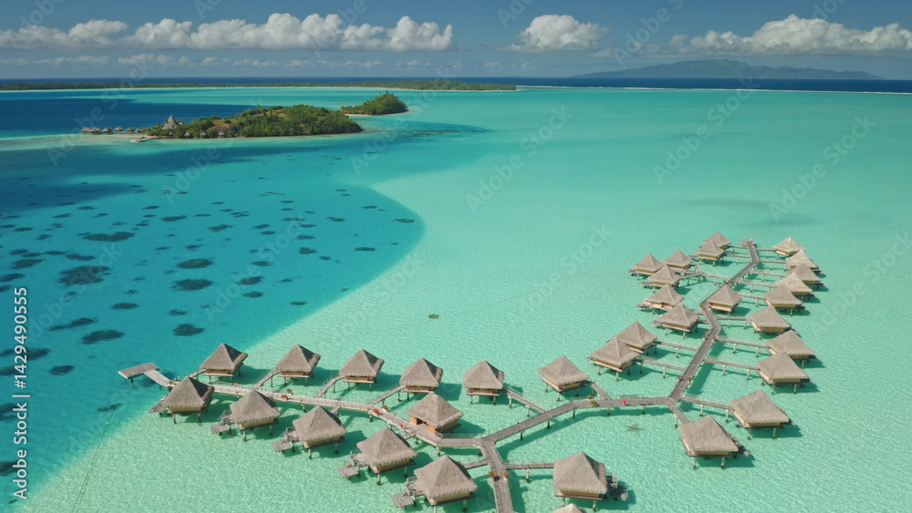 Luxury overwater bungalows resort invite for relaxation and escape. Crystal clear turquoise water, tropical island paradise. Exotic travel vacation getaway, romantic honeymoon. Aerial drone panorama.