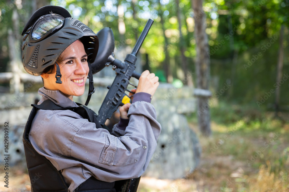 Fototapeta premium Portrait of pleased woman in uniform with paintball gun