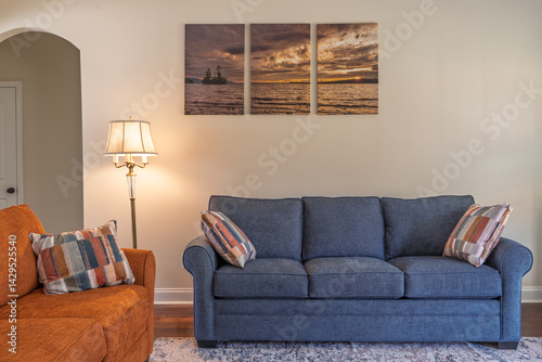 A living room with a blue couch and an orange chair. The couch is the main focus of the room and is surrounded by pillows. The room has a cozy and comfortable atmosphere