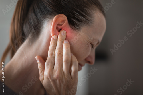 Young woman suffering from ear pain and tinnitus. Cause of earache includes otitis, earwax buildup.
