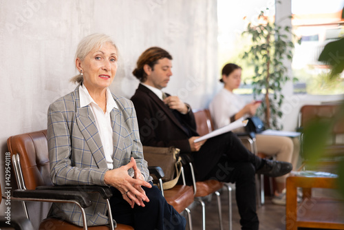 Elderly woman in business suit waiting on chair in office space