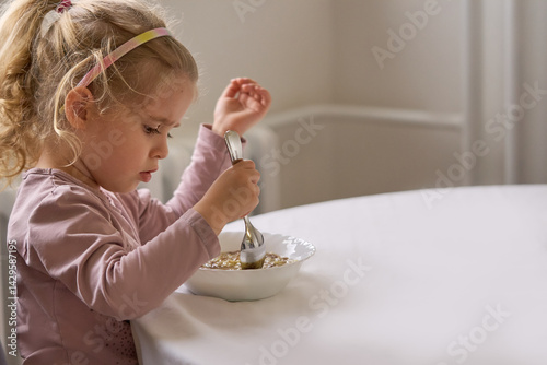 Cute todler girl focused, holding spoon and eating homemade soup at the dining rable with copy space     photo