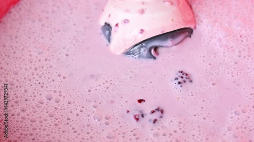 Close up of blending some dessert cream and some blackberries with blender in red pot on black table at home