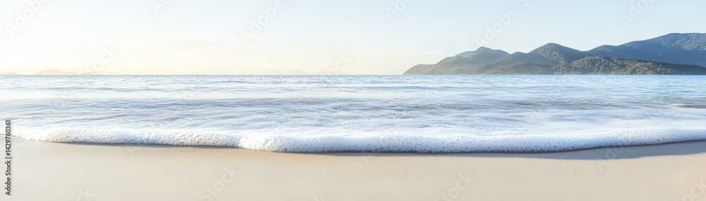 A serene beach scene with gentle waves lapping the shore, framed by distant mountains under a clear sky.