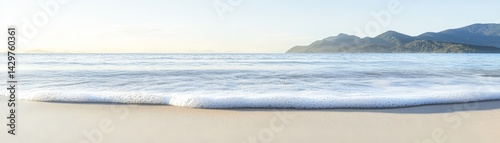 Obraz na płótnie A serene beach scene with gentle waves lapping the shore, framed by distant mountains under a clear sky. w salonie