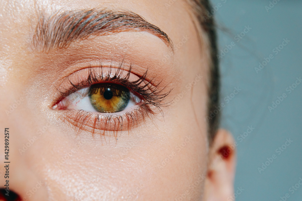 Close-up portrait of a woman showcasing her expressive green eyes and flawless skin against a soft blue background, capturing beauty and emotion.