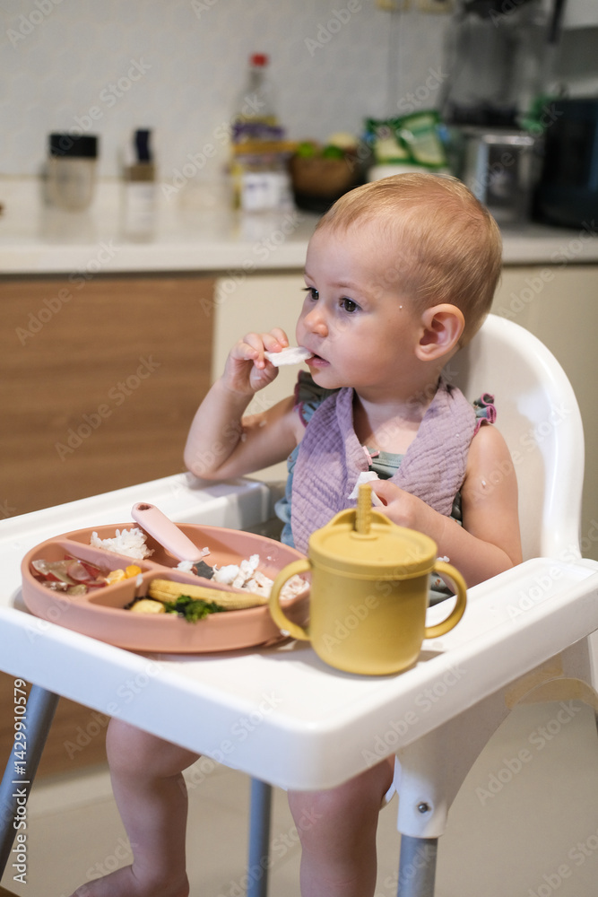 A little girl toddler is sitting on a high chair and eating a cracker. She plays with the cracker imagining that it is an airplane that flies into her mouth and bites is off. The baby plays with food A little girl toddler is sitting on a high chair and eating a cracker. She plays with the cracker imagining that it is an airplane that flies into her mouth and bites is off. The baby plays with food