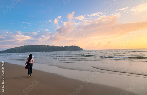 Female tourist enjoying a peaceful sunset stroll along Morjim Beach with golden light and soft waves in North Goa, India
