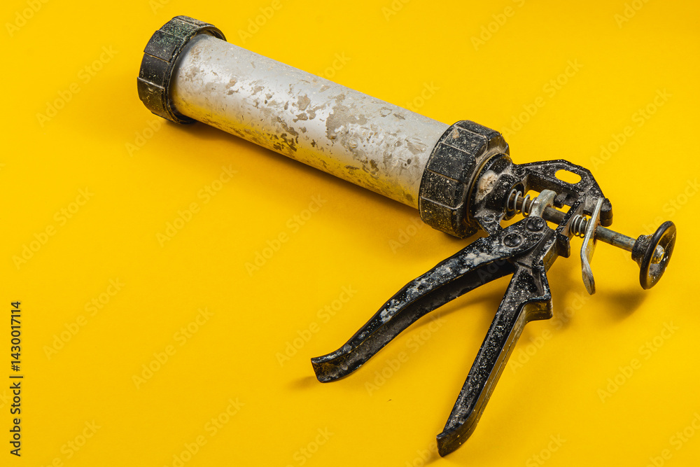Old caulking gun on a bright yellow background