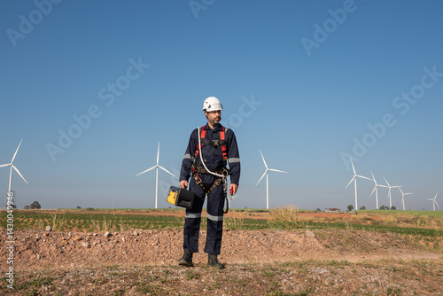 Engineer wearing uniform inspection and survey work in wind turbine farms rotation to generate electricity energy. Maintenance engineer working in wind turbine farm at sunset.