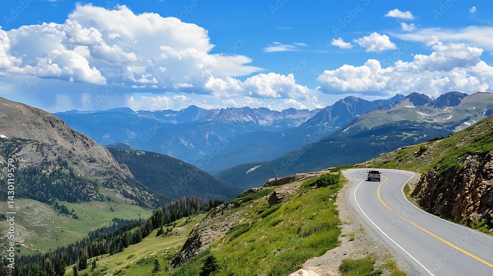 Naklejka premium Scenic mountain drive under a vast blue sky dotted with fluffy clouds, showcasing nature's grandeur and a winding road.