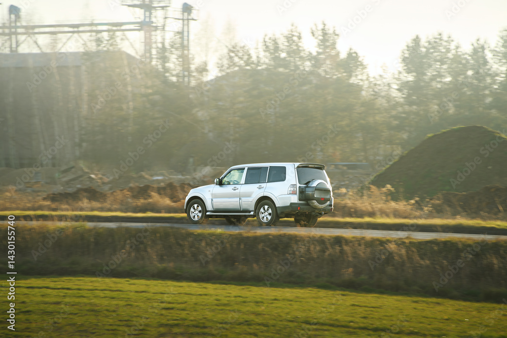 SUV speeding along an asphalt country road, surrounded by vibrant autumn foliage and forest