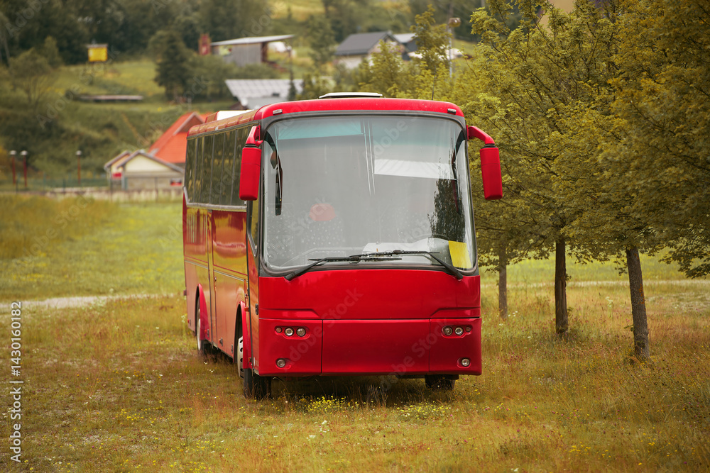 Red bus parked among trees with village houses in background