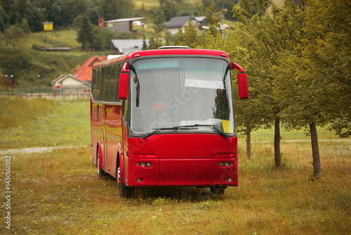 Obraz na płótnie Red bus parked among trees with village houses in background w salonie