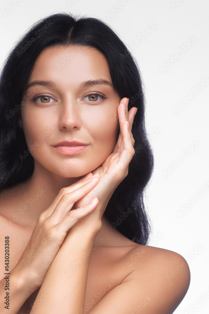 Beautiful young Caucasian woman with flawless skin gently touching her face. Conceptual portrait for skincare, beauty treatments, cosmetics promo or wellness advertisement.