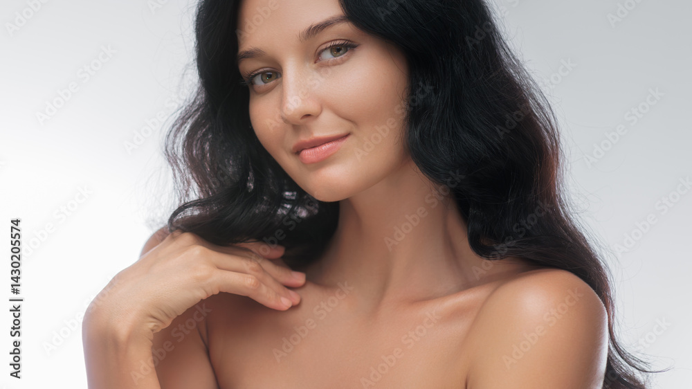 Elegant brunette woman with bare shoulders poses gracefully in a studio setting. Her soft smile and relaxed expression highlight her natural beauty, making this image ideal for beauty, skincare, and