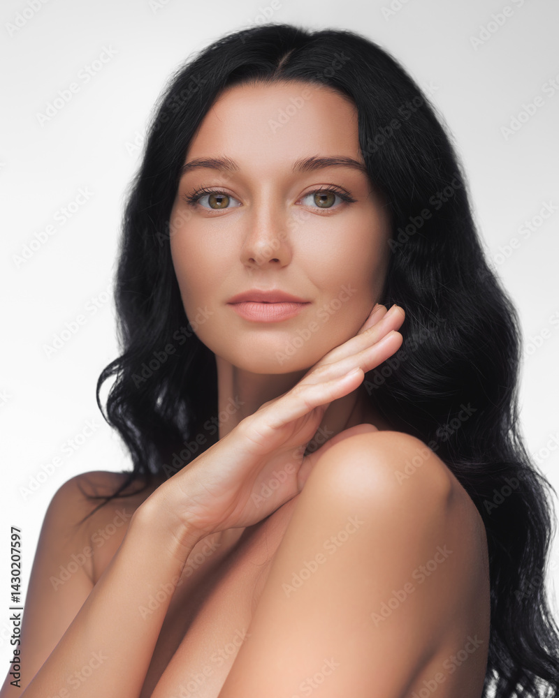 Beautiful Caucasian woman with flawless skin and long black hair poses gracefully in a beauty studio. Ideal for skincare, cosmetics, wellness, spa, or self-care promo concepts.