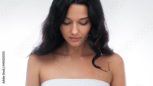 Obraz na płótnie Tranquil brunette woman wearing a white top is captured looking down in a serene studio portrait. The minimalist backdrop and soft lighting enhance her natural beauty, making this image ideal for w salonie
