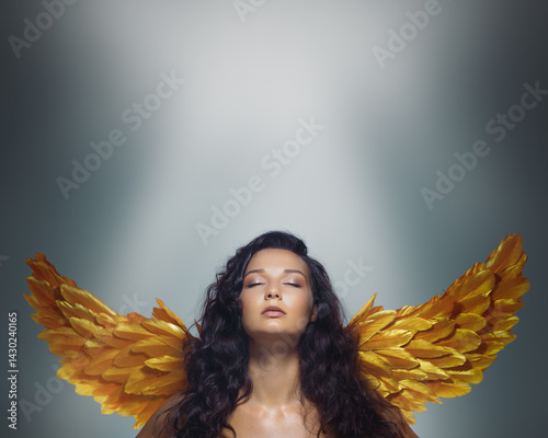 Obraz na płótnie Elegant brunette model with glowing skin and golden angel wings poses with closed eyes under soft light. A refined fantasy beauty banner with clear space for text and branding use. w salonie