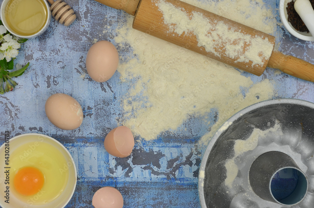 Flour and eggs on the table, top view blue kitchen table: flour, eggs, yolk, rolling pin, cake tin and delicacies.