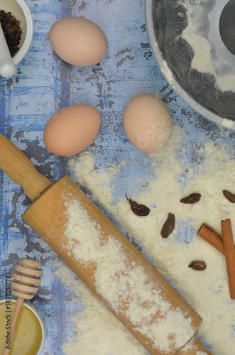 Baking ingredients for baking: flour, eggs, rolling pin, cake tin and delicacies on blue background. Top view blue, kitchen table.