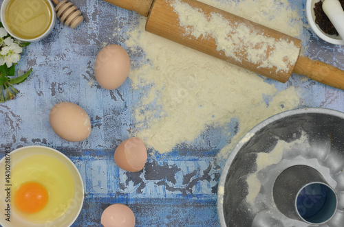 Obraz na płótnie Flour and eggs on the table, top view blue kitchen table: flour, eggs, yolk, rolling pin, cake tin and delicacies. w salonie
