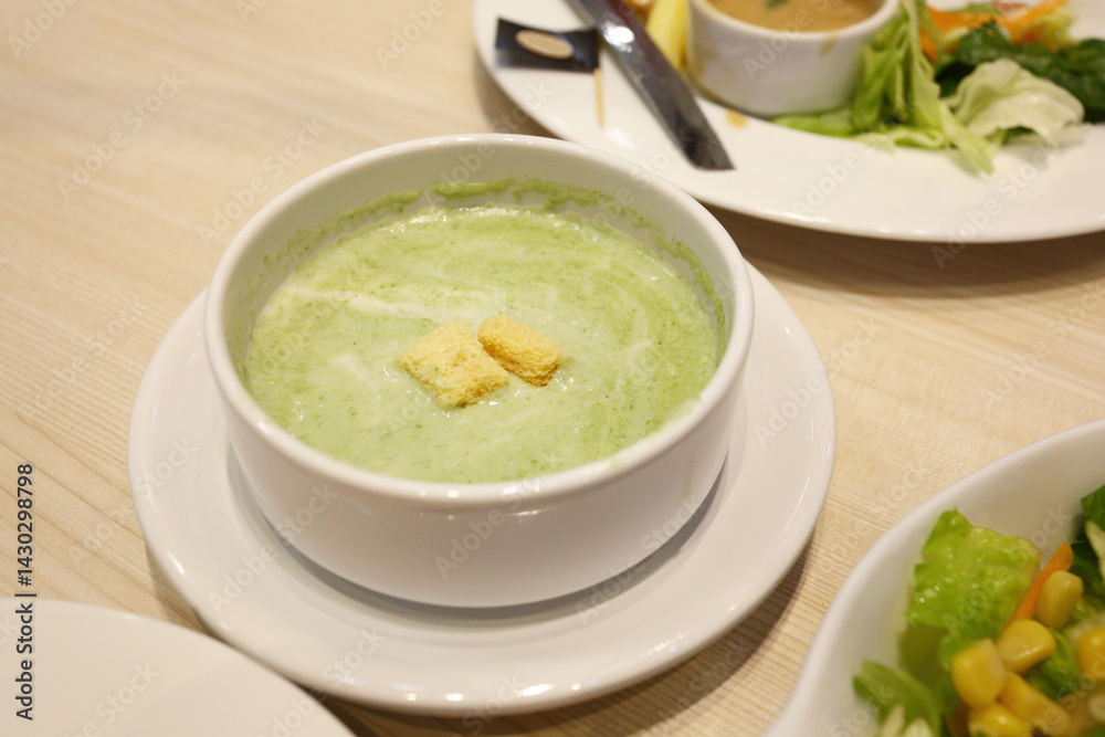 Green spinach soup in a white bowl with a saucer on the dining table.