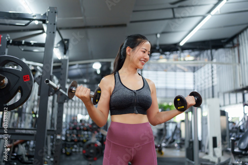 Young asian woman is working out her biceps with dumbbells in a modern, well equipped gym, demonstrating dedication to fitness and a healthy lifestyle