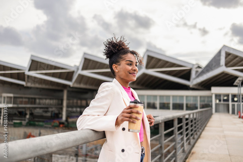 Woman in business attire holding coffee outdoors near modern architecture