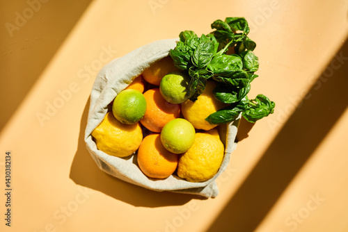 A reusable basket holds vibrant yellow lemons, oranges, and green limes, along with fresh basil leaves, promoting eco-friendly grocery shopping and healthy living.
