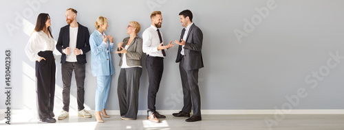 Fotografía Group of business professionals standing near gray wall in office engaged in lively conversation