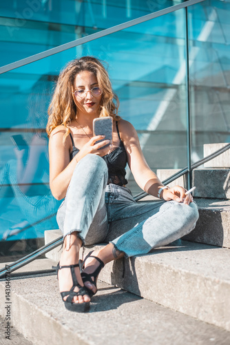 entspannte junge Frau mit smartphone und Zigarette sitzt auf einer Treppe