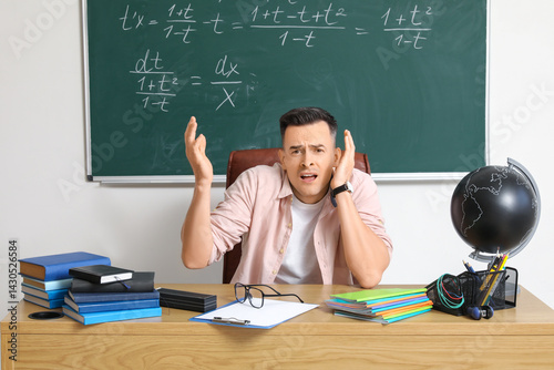 Stressed male teacher sitti...
