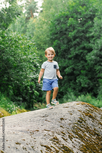 Little Boy Enjoying Playful Moment On Rock In Forest Outdoors