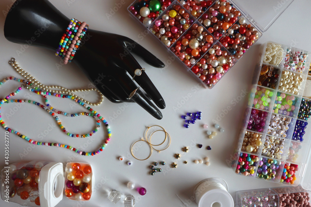 Hand figurine, colorful friendship bracelets, necklaces, various beads and DIY supplies on the table. Making jewelry at home. Flat lay.