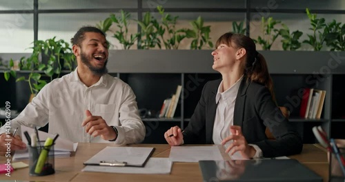 African office worker laughs and chats with a colleague at the table enjoying a casual conversation during a short work break