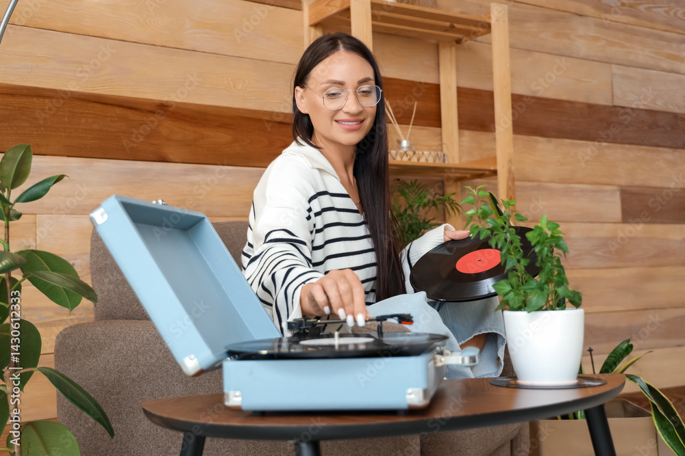 Fototapeta premium Beautiful woman in armchair using record player at home