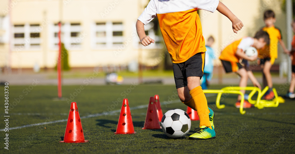 Obraz premium Football Boy in a Training Drill WIth Ball. Soccer Ball and Pylons on Turf Pitch. Youth Soccer Player Training. Young Footballer with Ball Training with Cones