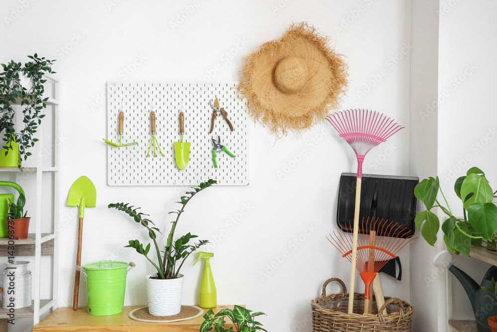 Bench, pegboard, basket with gardening tools and plants near white wall