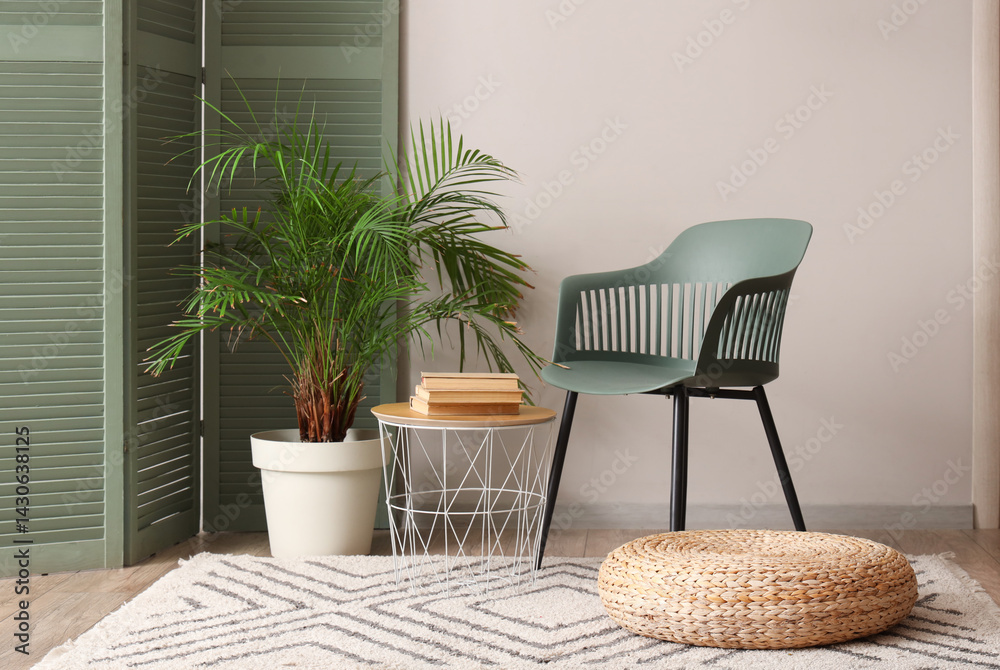 Fototapeta premium Chair, coffee table, folding screen and houseplant near white wall